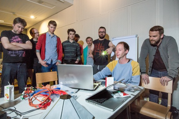 Group photo of all hackers and musicians looking at laptop