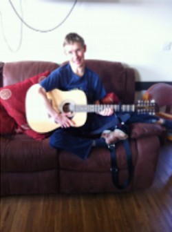 Image: Joe Rushbrook playing acoustic guitar and smiling
