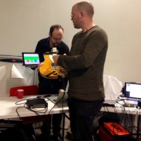 Gawain Hewitt demonstrating the Kellycaster in the foreground with Charles Matthews on laptop in the background