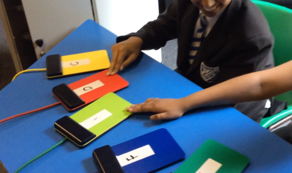 Two school children playing a selection of coloured switches laid out on a table.