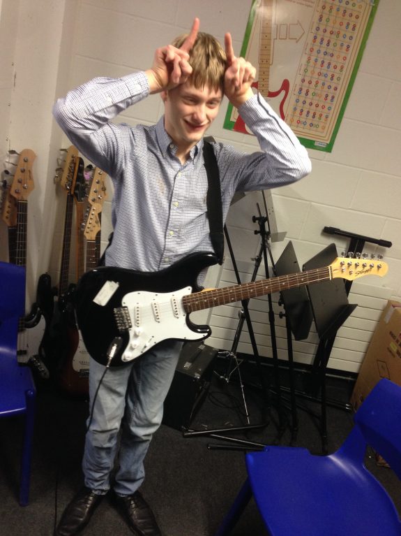 Young musician wearing electronic guitar pulls silly 'horns' pose for camera