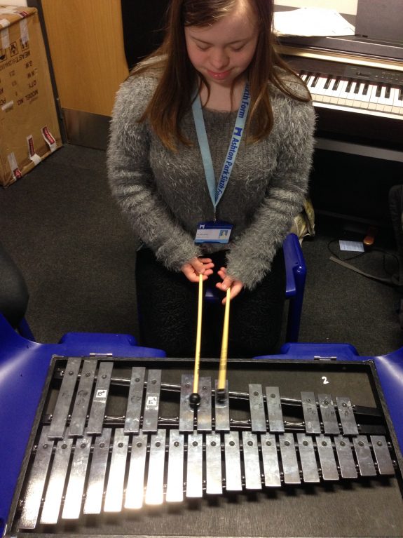 Young female musician kneels and plays glockenspiel