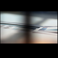 Image: still from video showing edges of printed paper photographs on a floor, with shadows cast upon them