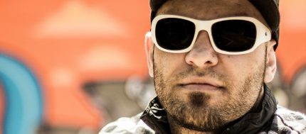 Close up on the face of rapper Billy Saga wearing white sunglasses and with a short beard