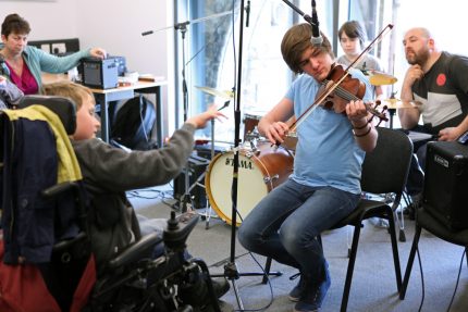 A young disabled musician conducts a jam session with a range of musicians and instruments