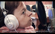 Image: still from Video showing close up of Sophie Partridge waering headphones and humming into studio microphone.