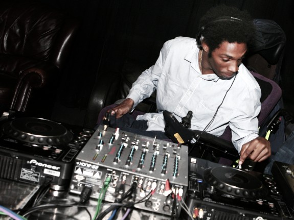 A young black man is DJing with decks and headphones