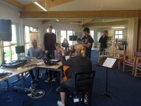 Three musicians playing together on the cello, iPad and Mixing Desks, while composers stand nearby, listening