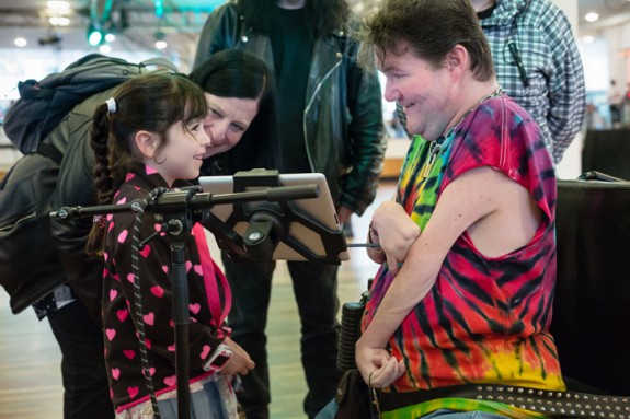 A young girl smiles at a Disabled musician as he shows her something on an ipad