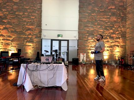 Colour photograph of Kris Halpin performing in a large room with computers, wires & mi mu gloves