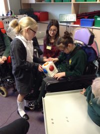 An older child helps a younger child to play a Skoog