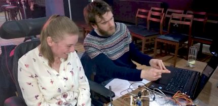 A maker and musician side by side looking at some music tech with lots of wires