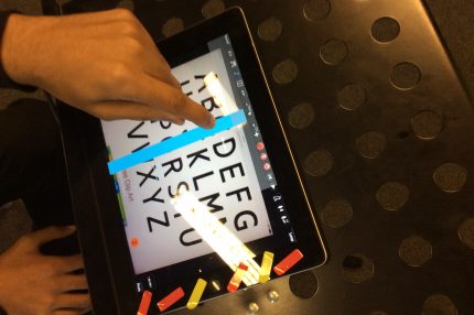 ipad with alphabet displayed and a person pressing the screen