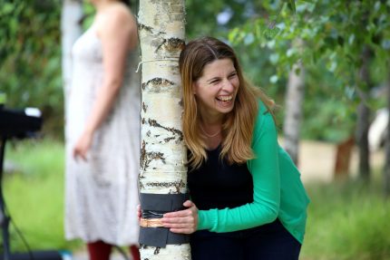 A woman smiles broadly as she hugs a tree and it makes a sound.