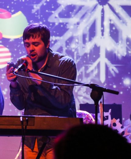 Louis performs onstage with keyboard & microphone and bold visuals