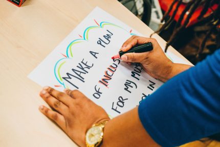 Two hands lean on a table as they draw a protest placard reading 