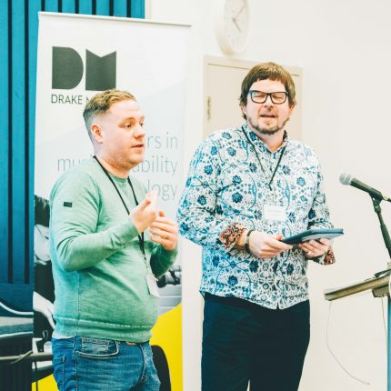 Matt Griffiths stands onstage in front of a microphone, next to a sign language interpreter