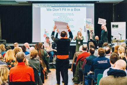 People walk down the centre aisle of the audience holding signs in the air
