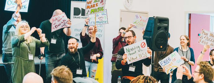 The Drake Music team are staging a protest with colourful signs onstage at a conference