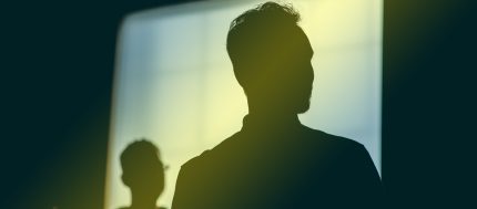 Two figures are silhouetted against a window with a yellow light overlaying it