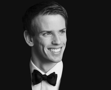 A formal portrait of Ewan who smiles as he looks off-camera. He is wearing a tuxedo and bowtie and his hair is neatly combed to one side.