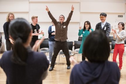 Ben stands triumphantly conducting the group with both hands in the air
