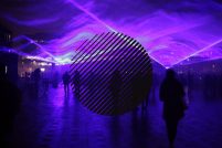 A mysterious image of blues and purples, laser lights create shapes in smoke and people are seen walking in silhouette