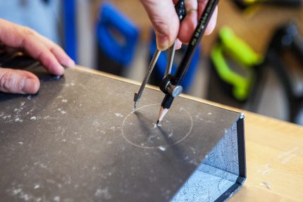 A compass is being used to draw and score a circle on the front of a lever arch folder