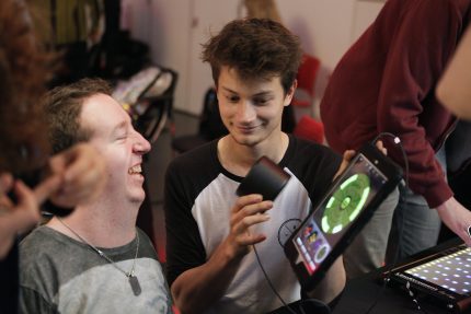 Two men are playing music with an iPad and smiling