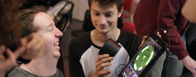 Two men are playing music with an iPad and smiling