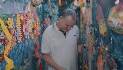 A man looks down and smiles as he dances in a colourful space decorated with papier mache