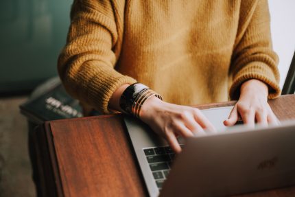 Woman wearing mustard jumper uses a laptop