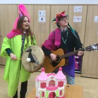 Two musicians play instruments, both are wearing eccentric brightly coloured clothes.