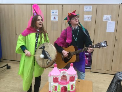 Two musicians play instruments, both are wearing eccentric brightly coloured clothes.