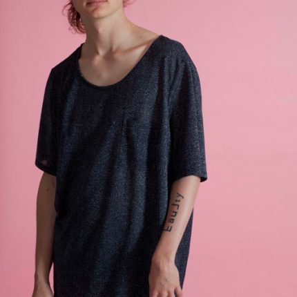 We can see a cropped image of a person's body, wearing a scoop neck grey jersey top and with the word fault tattooed on their arm. They are white and slim.