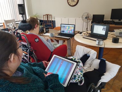 Two Disabled women are playing music using technology. One plays an iPad the other makes music using her eyes with a computer.