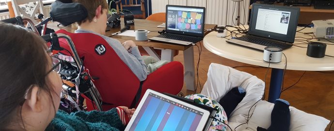 Two Disabled women are playing music using technology. One plays an iPad the other makes music using her eyes with a computer.