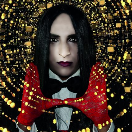 Patrick is facing us directly in this creative image. He wears a bow tie and white shirt, red gloves and his hands are making a frame under his face. There are gold spirals all around