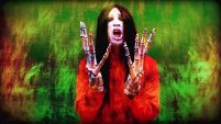 Still from a music video showing a man with a pale fave and long black hair, his hands are like large skeleton hands.
