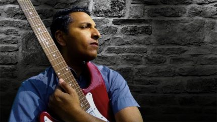 An Asian man holding an electric guitar