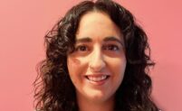 Deborah, a smiling white Mediterranean woman with dark brown hair that reaches just below her shoulders.