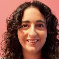 Deborah, a smiling white Mediterranean woman with dark brown hair that reaches just below her shoulders.