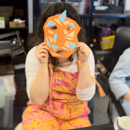 Photograph of Daisy Higman wearing a colourful orange jumpsuit wearing an orange mask.