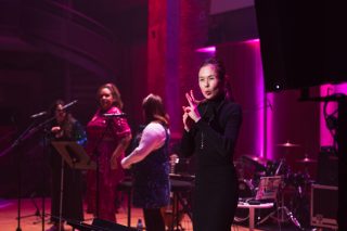 BSL interpreter on stage during Daisy Highman's performance with her band. The back lighting is pink.