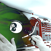 Overhead view of analogue turntables, with added colouring in purple, green, pink and red. Two hands are seen adjusting a record on one of the turntables.