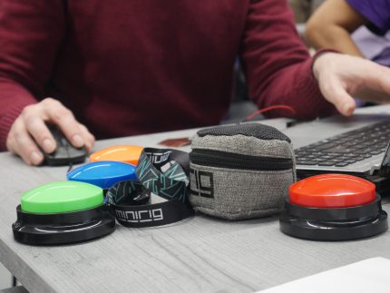 Blue, green, red and orange dog training buttons lined up on a table being used as accessible instruments.