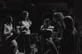A black and white group picture of 5 people, our Emergent Artists, plus a support technician. The group are in conversation, the picture is very natural.