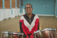 A Disabled adult sits in front of two timpani drums. They are sat in a large empty room.