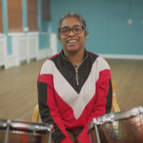 A Disabled adult sits in front of two timpani drums. They are sat in a large empty room.