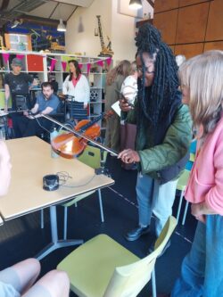 A young black woman bows the Touch Violin: a DM OrchLab accessible violin mounted to a table